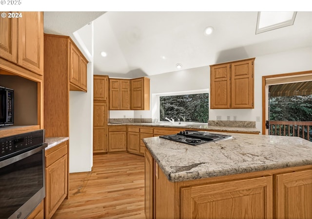 kitchen with light stone countertops, gas stovetop, a kitchen island, light hardwood / wood-style flooring, and oven