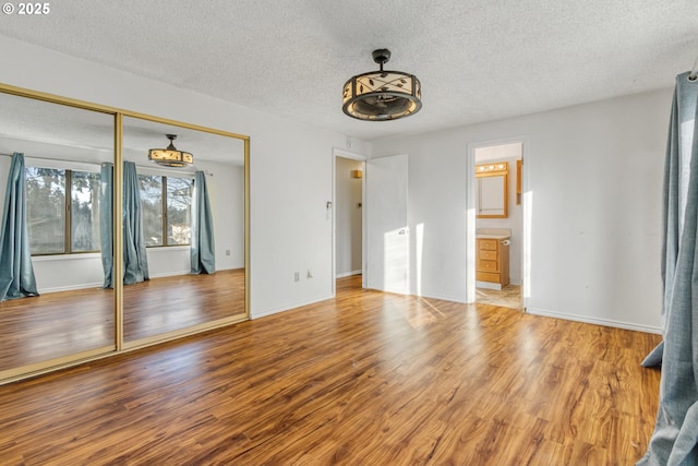 unfurnished bedroom featuring a textured ceiling, ensuite bathroom, a closet, and hardwood / wood-style floors