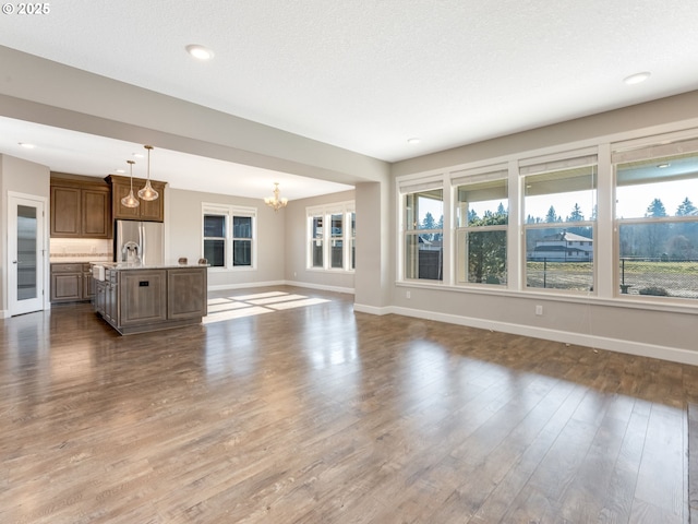 unfurnished living room with an inviting chandelier, a textured ceiling, and dark hardwood / wood-style flooring