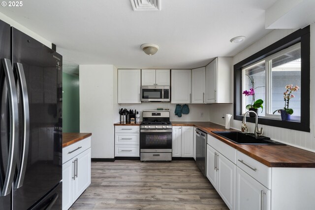 567 NW Cedar Ct, Warrenton, OR 97146 - kitchen featuring butcher block counters, appliances with stainless steel finishes, white cabinetry, and light wood-style flooring
