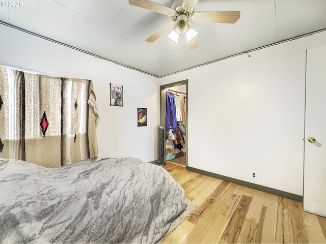 bedroom featuring baseboards, a ceiling fan, wood finished floors, a walk in closet, and a closet