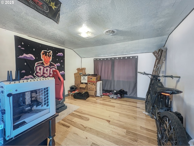 interior space with a textured ceiling, visible vents, vaulted ceiling, and wood finished floors