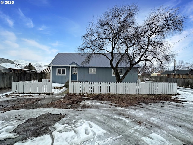 snow covered rear of property featuring a fenced front yard and metal roof