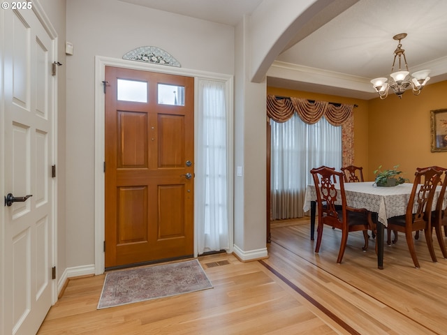 foyer entrance featuring visible vents, baseboards, light wood-style flooring, an inviting chandelier, and arched walkways