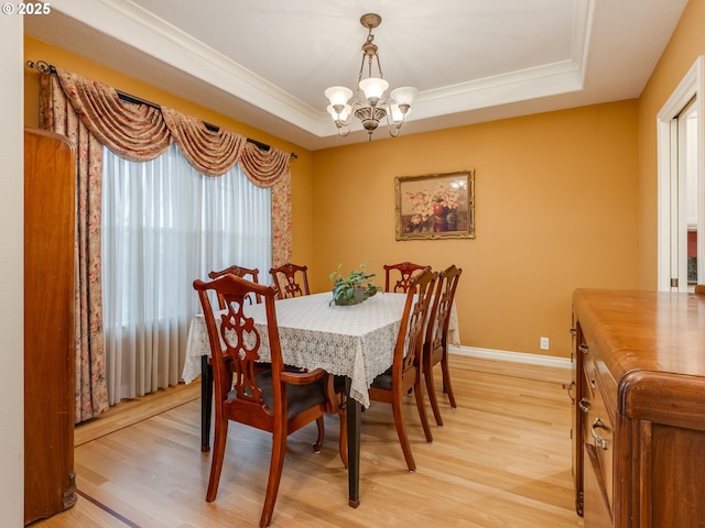 dining space with baseboards, light wood finished floors, an inviting chandelier, a tray ceiling, and ornamental molding