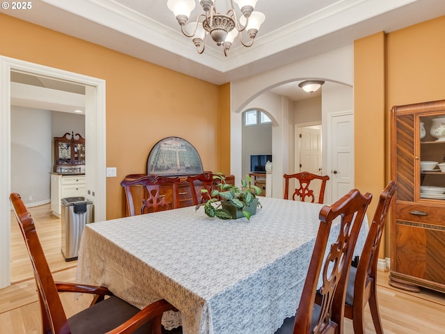 dining room with light wood-style flooring, ornamental molding, arched walkways, an inviting chandelier, and baseboards