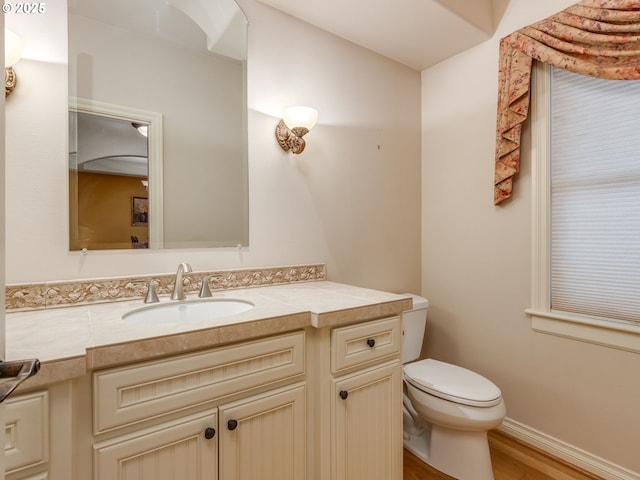 half bath featuring vanity, toilet, wood finished floors, and baseboards