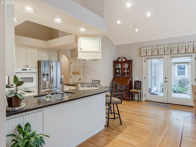 kitchen featuring light wood-type flooring, a sink, dark stone countertops, appliances with stainless steel finishes, and a peninsula