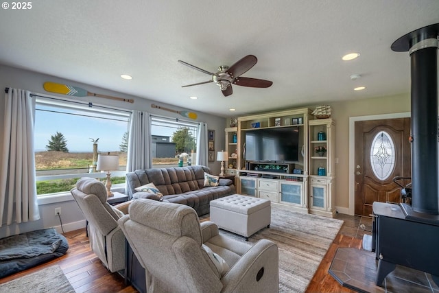 7655 Elliott St, Bay City, OR 97107 - living room featuring a wood stove, ceiling fan, wood finished floors, and a healthy amount of sunlight