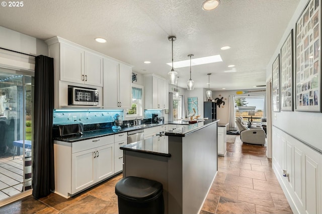 7655 Elliott St, Bay City, OR 97107 - kitchen with white cabinets, dark countertops, appliances with stainless steel finishes, a peninsula, and a skylight