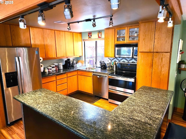 kitchen with sink, light hardwood / wood-style flooring, stainless steel appliances, a center island, and dark stone counters