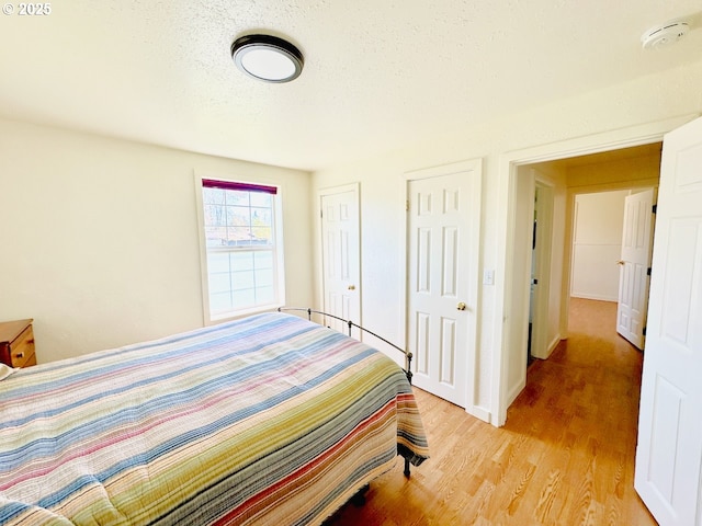 bedroom featuring light wood-style floors, two closets, a textured ceiling, and baseboards