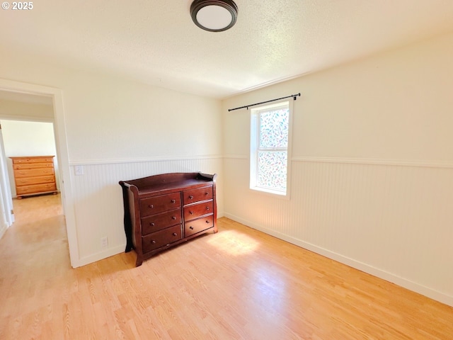 unfurnished bedroom with wood finished floors, a textured ceiling, a wainscoted wall, and baseboards