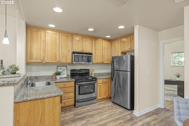 kitchen featuring sink, light stone counters, pendant lighting, stainless steel appliances, and light hardwood / wood-style floors