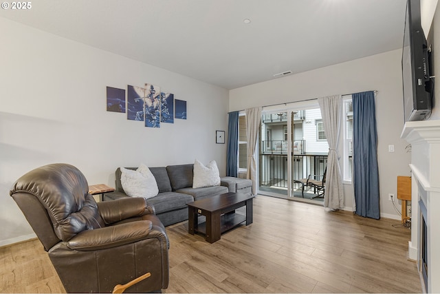 living room featuring a fireplace, visible vents, light wood finished floors, and baseboards