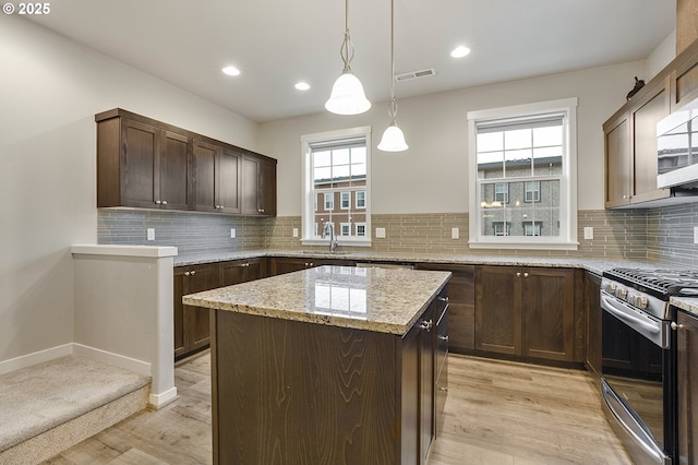 kitchen with visible vents, a kitchen island, a sink, dark brown cabinets, and appliances with stainless steel finishes