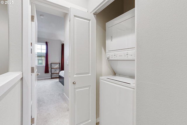 laundry area with baseboards, light carpet, laundry area, a textured wall, and stacked washer / drying machine