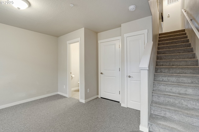 stairway with carpet flooring, visible vents, a textured ceiling, and baseboards