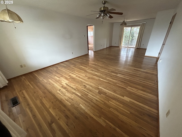 empty room featuring arched walkways, visible vents, a ceiling fan, and wood finished floors