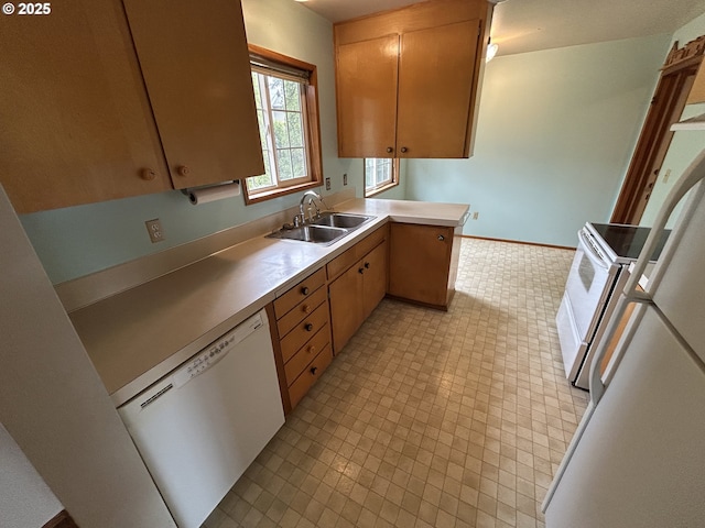 kitchen featuring baseboards, light countertops, a peninsula, white appliances, and a sink