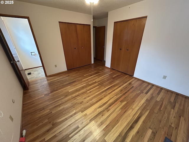 unfurnished bedroom with light wood finished floors, two closets, and a textured ceiling