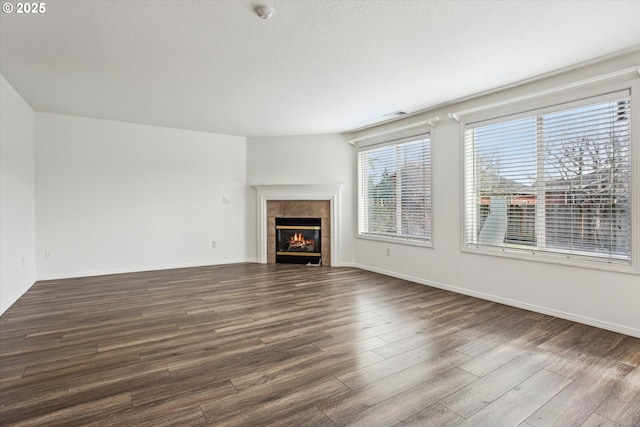 unfurnished living room featuring a tiled fireplace, a textured ceiling, and dark hardwood / wood-style flooring