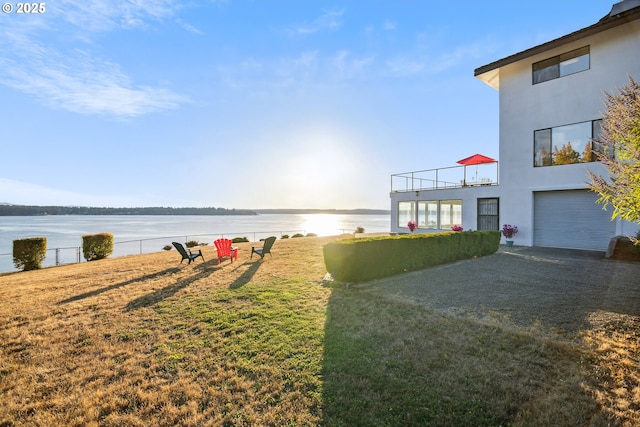 view of yard with a water view, a garage, and a balcony