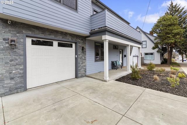 exterior space with a garage, stone siding, a porch, and concrete driveway