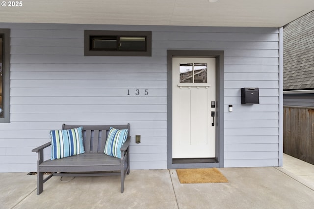 view of exterior entry featuring a shingled roof and fence