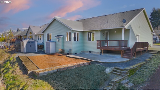 back house at dusk with a storage shed, a patio area, and a wooden deck