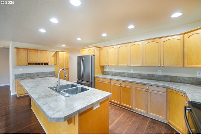 kitchen with dark wood-type flooring, sink, a center island with sink, stainless steel refrigerator, and stove