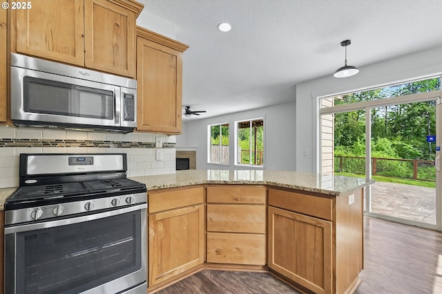 kitchen featuring stainless steel appliances, a ceiling fan, a peninsula, wood finished floors, and backsplash