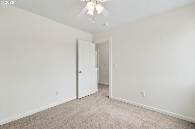 empty room featuring light colored carpet, a ceiling fan, and baseboards
