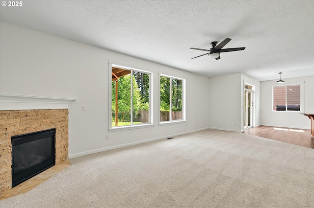 unfurnished living room featuring ceiling fan, carpet floors, a textured ceiling, baseboards, and a fireplace with flush hearth