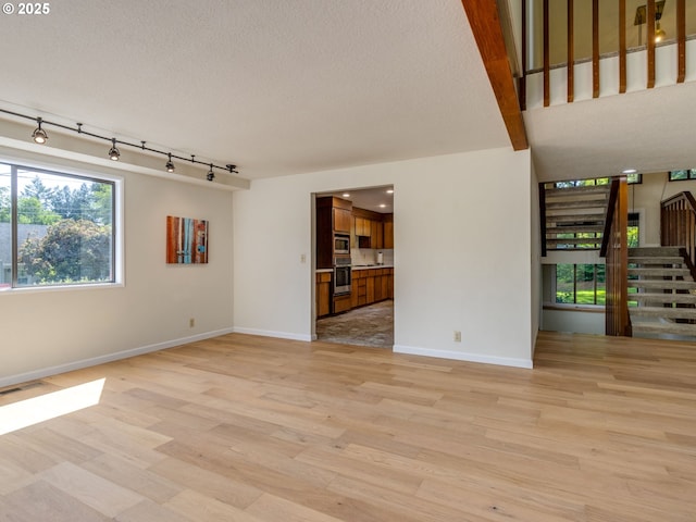 7785 SW W Slope Dr, Portland, OR 97225 - unfurnished living room featuring stairway, light wood-type flooring, a textured ceiling, and track lighting
