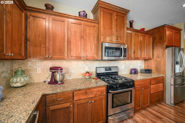 2356 Benjamin Ave, Salem, OR 97304 - kitchen featuring stainless steel appliances, light wood-style flooring, a textured ceiling, light stone counters, and backsplash