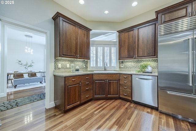 kitchen featuring light stone counters, stainless steel appliances, a sink, light wood-style floors, and backsplash