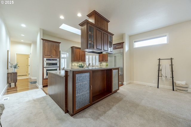 kitchen featuring stainless steel appliances, a skylight, a sink, and light colored carpet