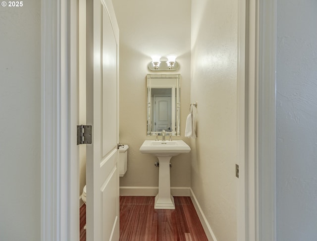 half bathroom with baseboards and wood finished floors