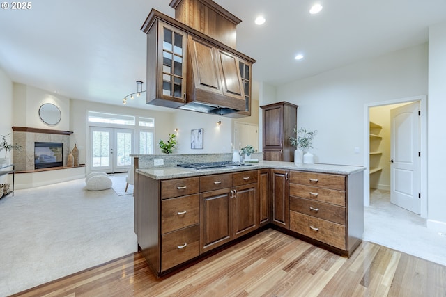 kitchen featuring light carpet, light stone counters, glass insert cabinets, light wood-style floors, and stainless steel gas cooktop