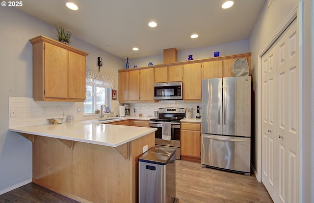 kitchen with sink, kitchen peninsula, stainless steel appliances, light hardwood / wood-style floors, and backsplash