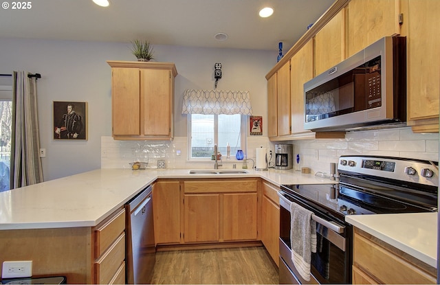 kitchen featuring sink, stainless steel appliances, tasteful backsplash, kitchen peninsula, and light wood-type flooring