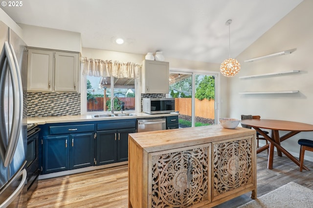 kitchen with pendant lighting, sink, appliances with stainless steel finishes, vaulted ceiling, and light wood-type flooring