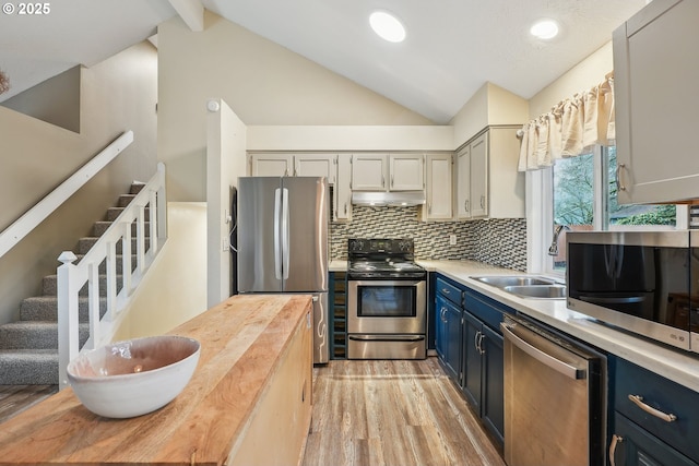 kitchen featuring appliances with stainless steel finishes, tasteful backsplash, lofted ceiling, sink, and blue cabinetry