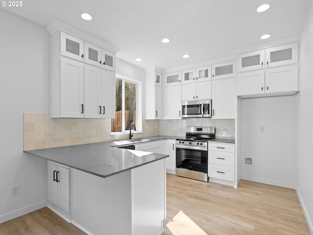 kitchen with appliances with stainless steel finishes, a peninsula, a sink, recessed lighting, and white cabinetry
