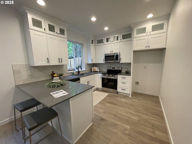 kitchen featuring stainless steel appliances, a sink, a peninsula, baseboards, and recessed lighting