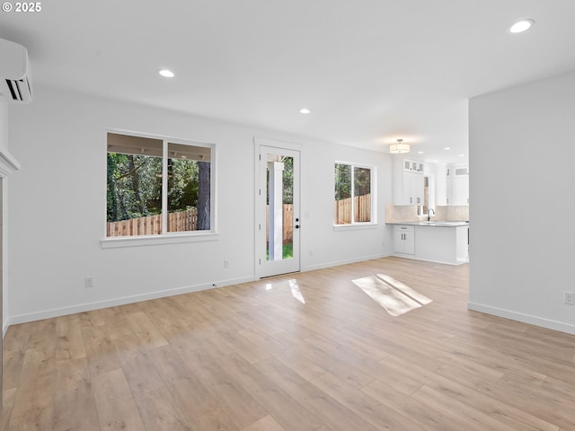 unfurnished living room with plenty of natural light, a wall unit AC, light wood finished floors, and recessed lighting