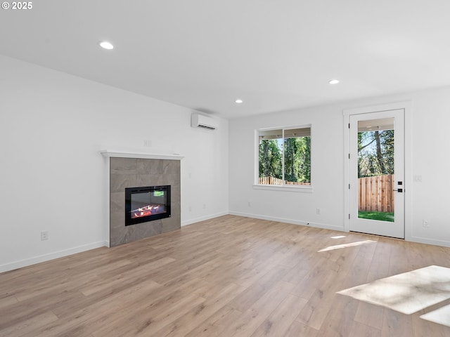 unfurnished living room featuring an AC wall unit, light wood-style floors, a tiled fireplace, recessed lighting, and baseboards