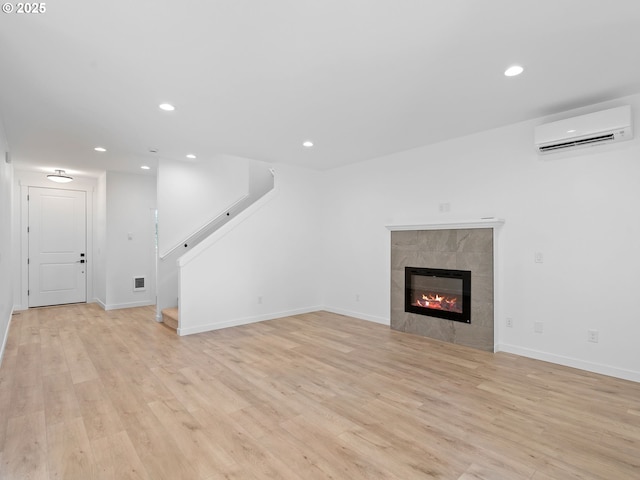 unfurnished living room featuring a wall unit AC, recessed lighting, light wood-style flooring, stairs, and a fireplace