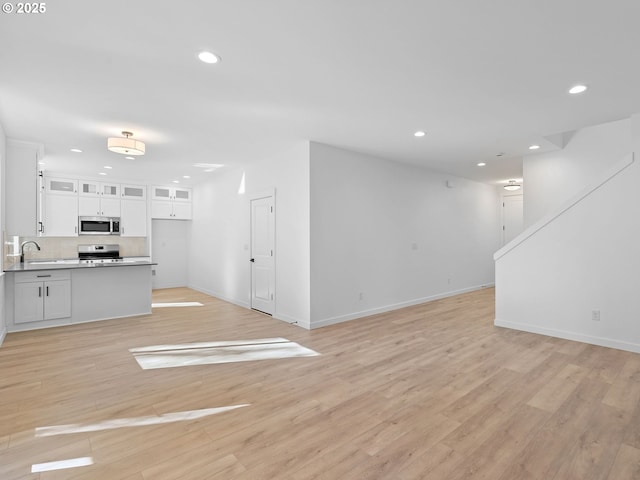 unfurnished living room with recessed lighting, baseboards, light wood-type flooring, and a sink